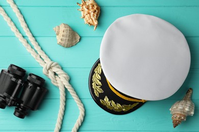 Peaked cap, rope, shells and binoculars on turquoise wooden background, flat lay