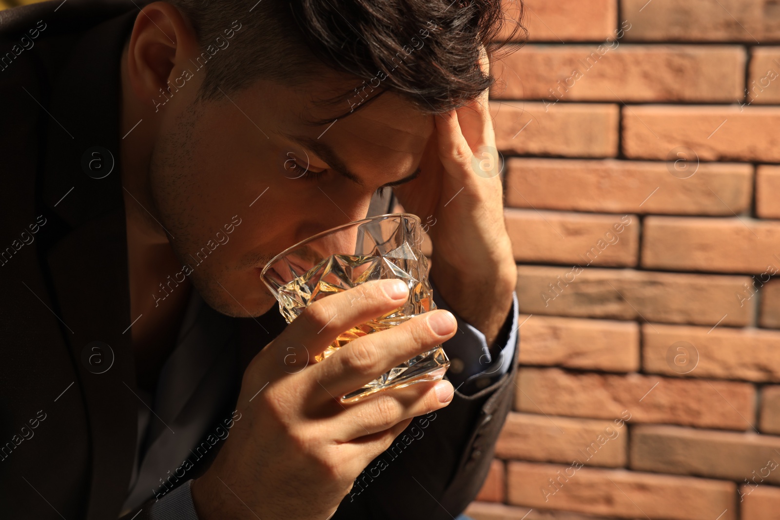 Photo of Addicted man drinking alcohol near red brick wall, closeup