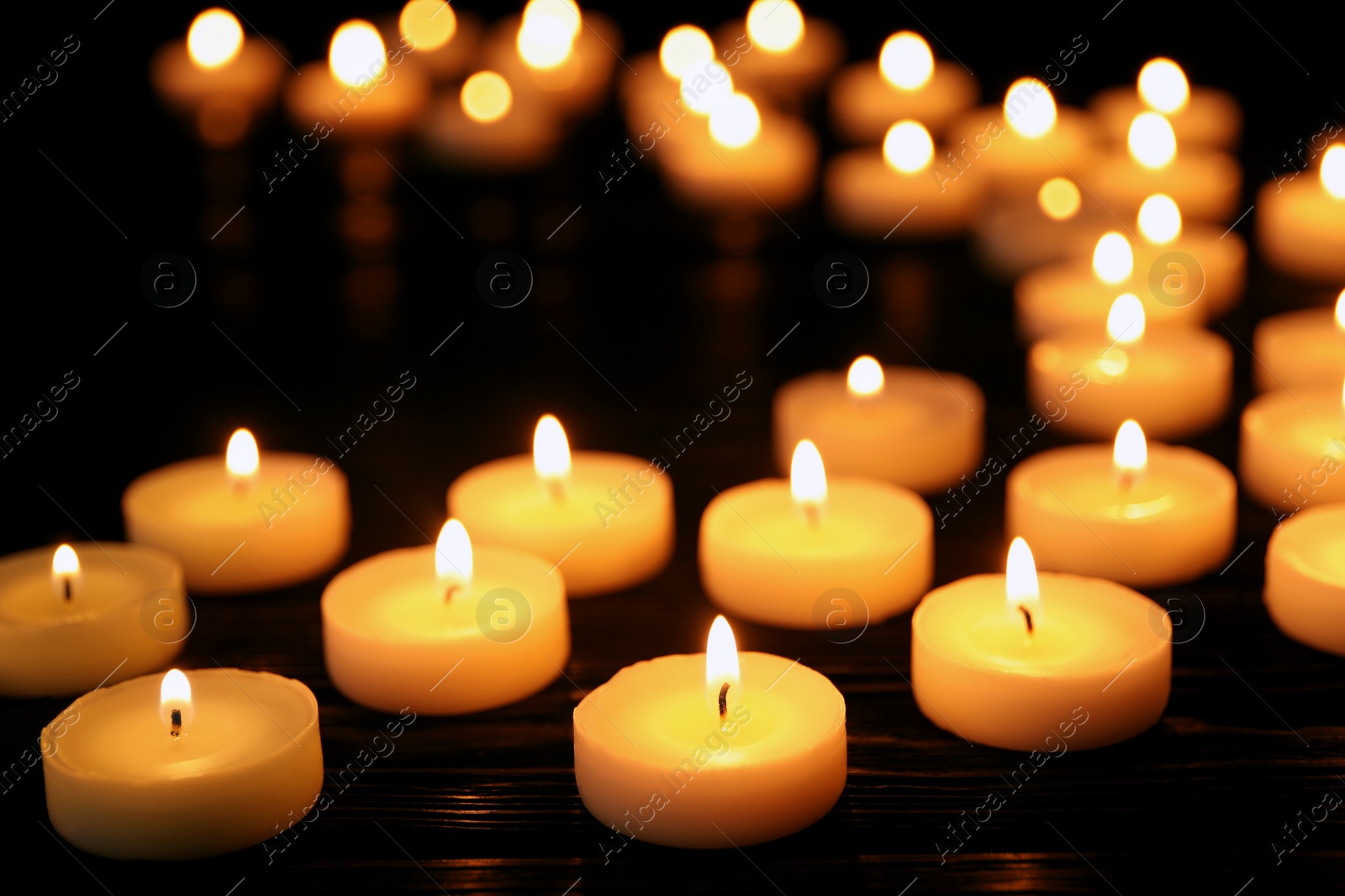 Photo of Many burning candles on black table in darkness