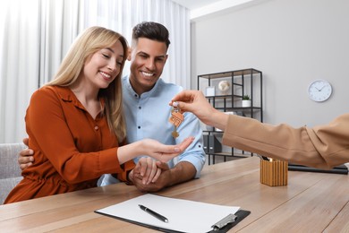 Real estate agent giving house key to couple at table in office