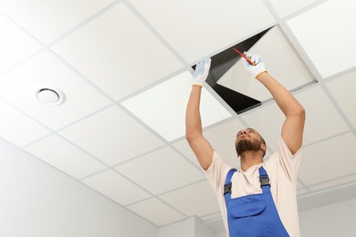 Photo of Electrician with screwdriver repairing ceiling light indoors, low angle view. Space for text