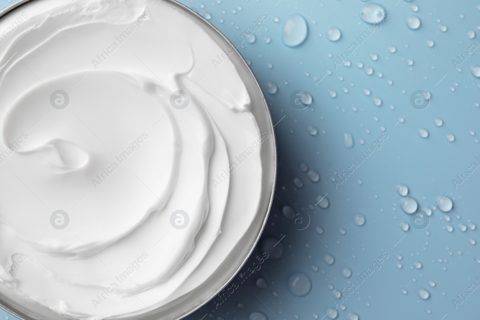 Photo of Jar of face cream on light blue surface covered with water drops, top view. Space for text