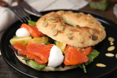 Photo of Tasty bagel with salmon, mozzarella cheese, tomatoes and lettuce on wooden table, closeup