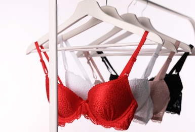 Photo of Hangers with beautiful lace bras on rack against white background. Stylish underwear