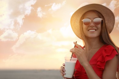 Photo of Beautiful young woman with tasty milk shake outdoors, space for text