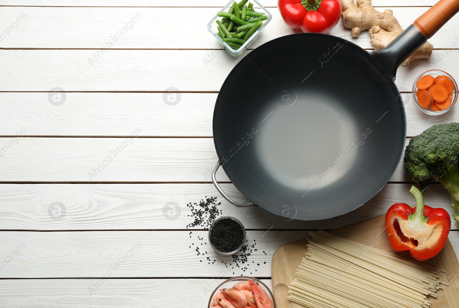 Photo of Empty iron wok and raw ingredients on white wooden table, flat lay. Space for text