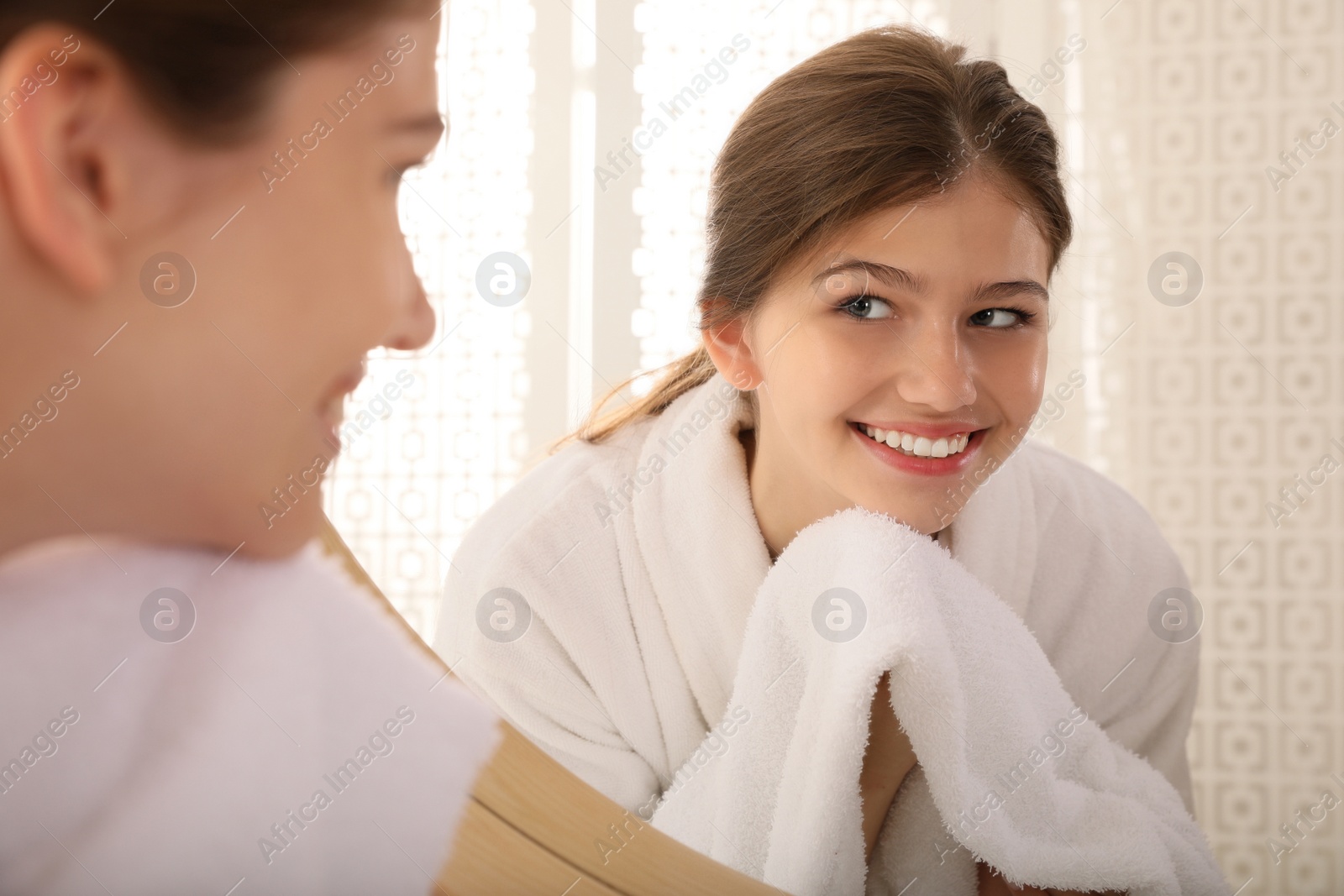 Photo of Beautiful teenage girl wiping face with towel near mirror at home