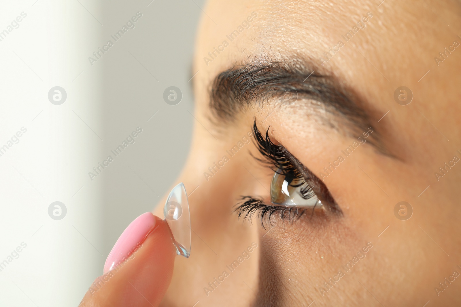 Photo of Young woman putting contact lens in her eye, closeup