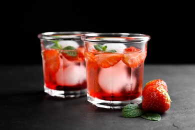 Photo of Delicious cocktails with strawberries, mint and ice balls on black table
