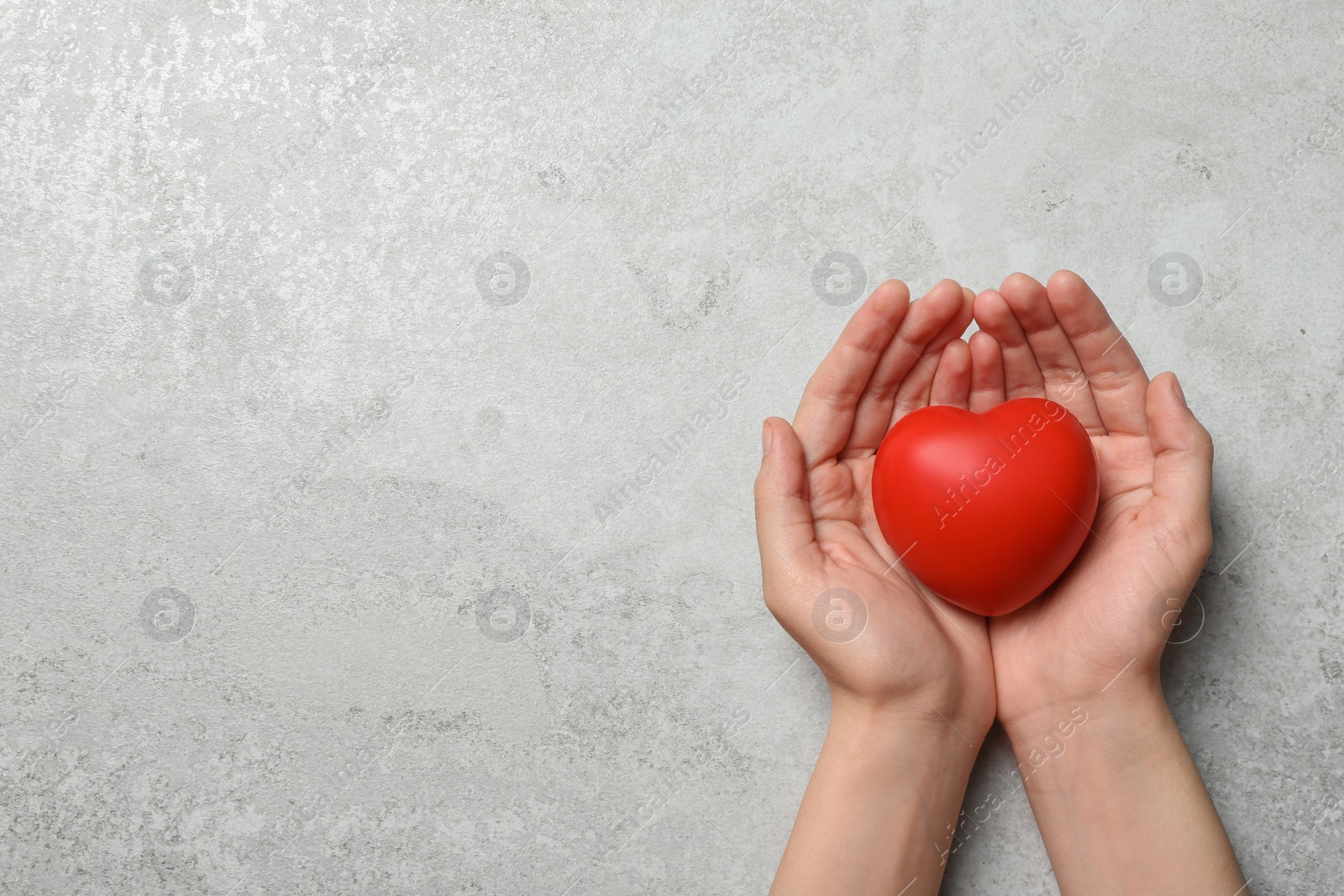 Photo of Woman holding heart on grey stone background, top view with space for text. Donation concept