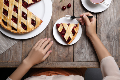 Photo of Woman eating delicious cherry pie at wooden table, top view