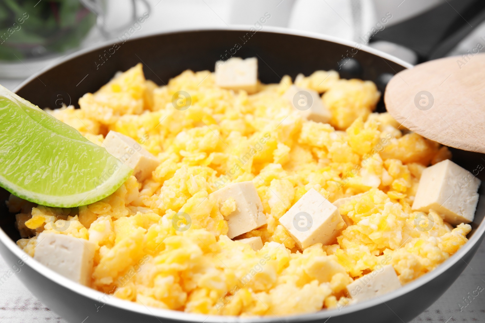 Photo of Frying pan with delicious scrambled eggs, tofu and lime, closeup