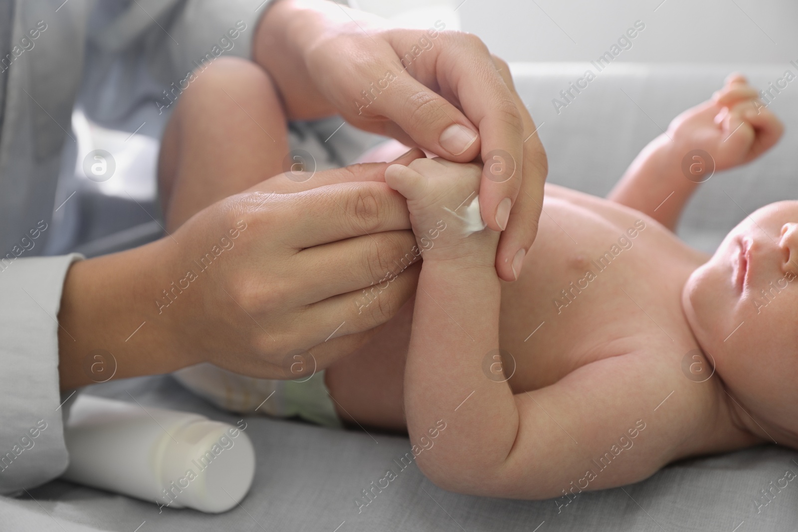 Photo of Mother applying moisturizing cream onto baby`s hand on changing table, closeup