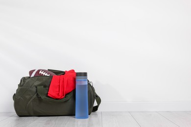 Photo of Gym bag and sports equipment on floor near white wall, space for text