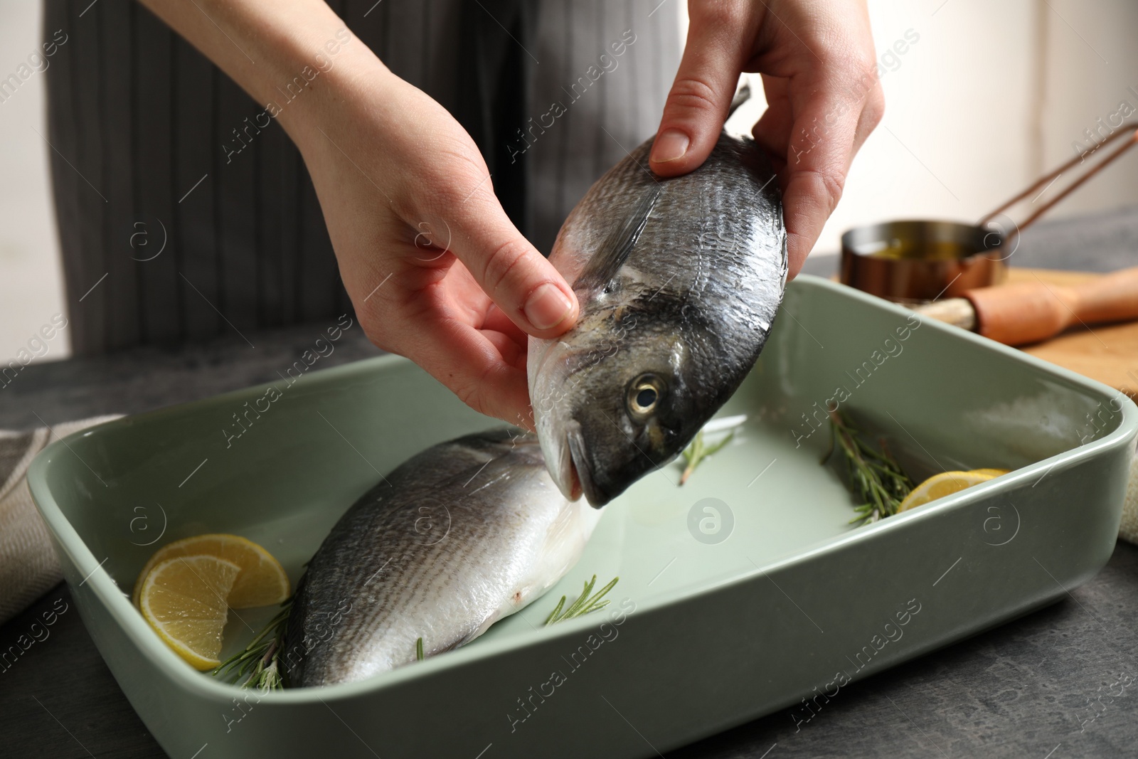 Photo of Woman putting dorada fish into baking dish, closeup