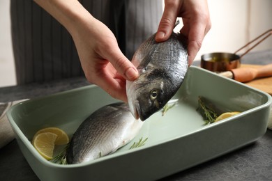 Woman putting dorada fish into baking dish, closeup