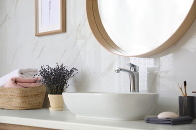 Bathroom counter with vessel sink, flowers and towels in bathroom interior. Idea for design