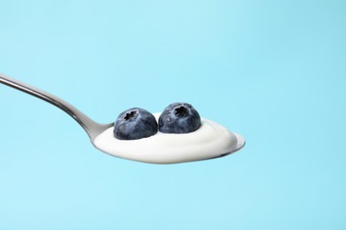 Photo of Spoon with yogurt and blueberries on light blue background, closeup