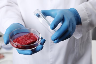 Scientist holding Petri dish with raw cultured meat in laboratory, closeup
