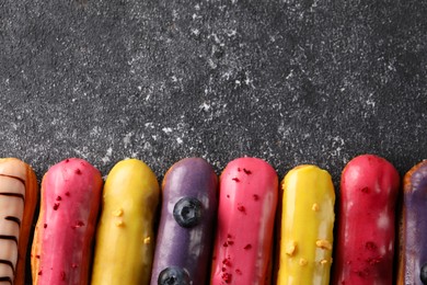 Photo of Different tasty glazed eclairs on dark textured table, flat lay. Space for text