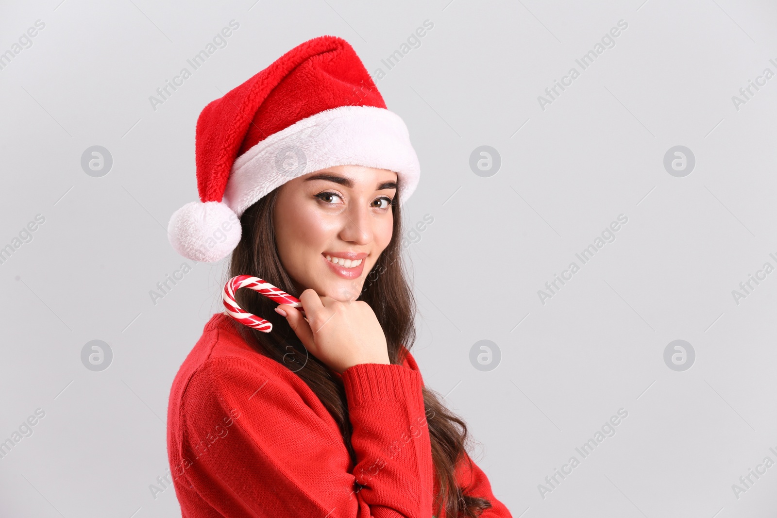Photo of Beautiful woman in Santa Claus hat holding candy cane on light grey background. Space for text