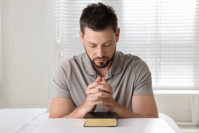 Photo of Religious man with Bible praying at home