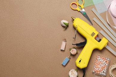 Photo of Hot glue gun and handicraft materials on brown background, flat lay. Space for text