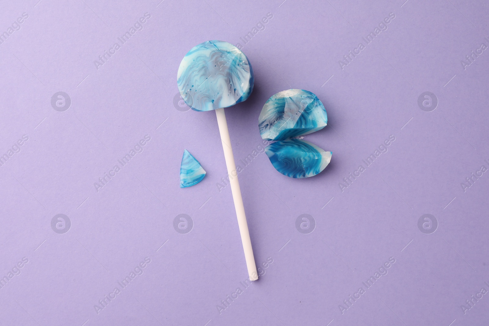 Photo of Broken lollipop on violet background, flat lay