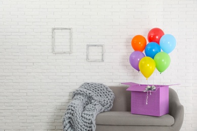 Photo of Gift box with bright air balloons on sofa against white brick wall. Space for text