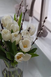Beautiful bouquet of willow branches and tulips in kitchen sink