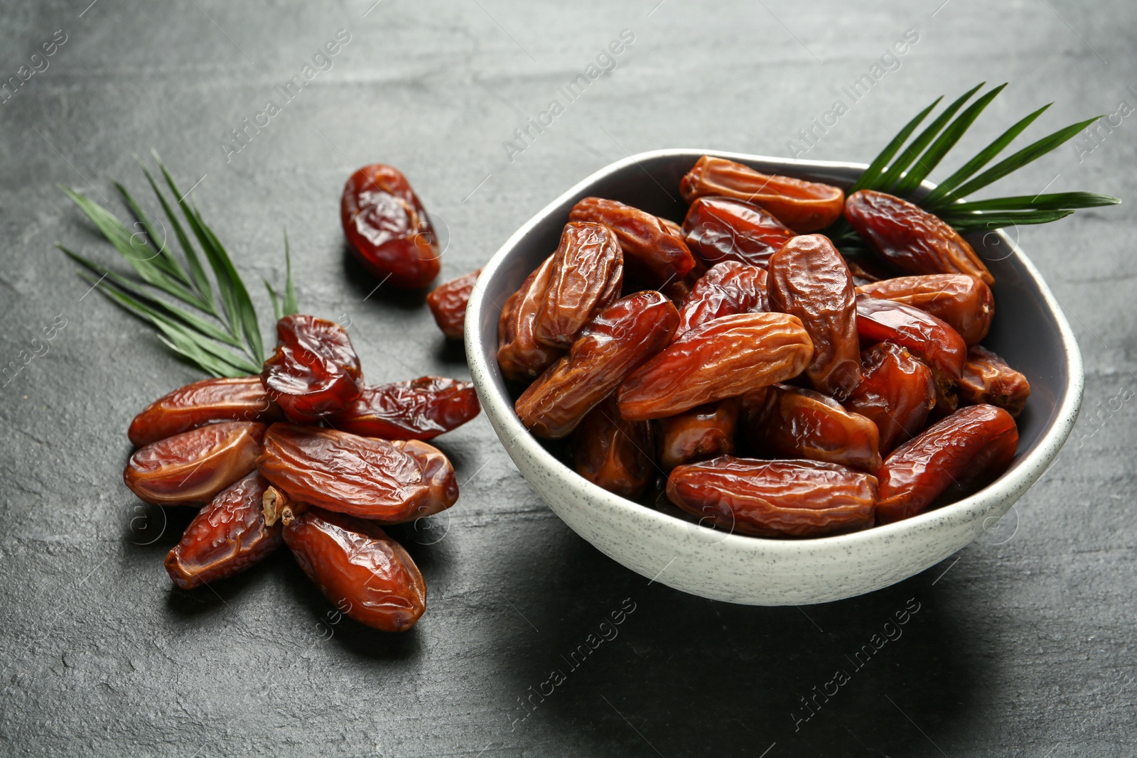 Photo of Tasty sweet dried dates and green leaves on black table