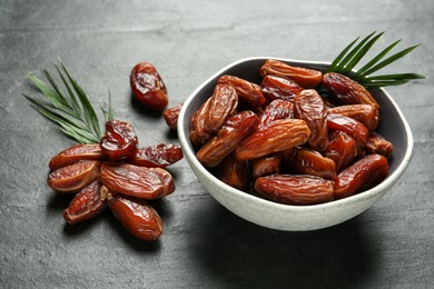 Photo of Tasty sweet dried dates and green leaves on black table