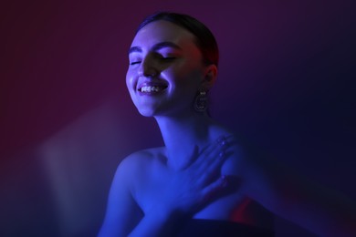 Portrait of beautiful young woman on color background in neon lights