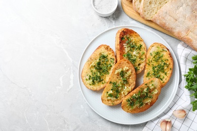 Photo of Slices of toasted bread with garlic and herb on light grey marble table, flat lay. Space for text