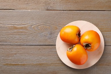 Photo of Delicious ripe persimmons on wooden table, top view. Space for text