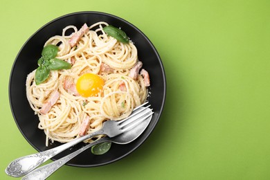 Photo of Delicious pasta Carbonara with egg yolk and cutlery on light green background, top view. Space for text
