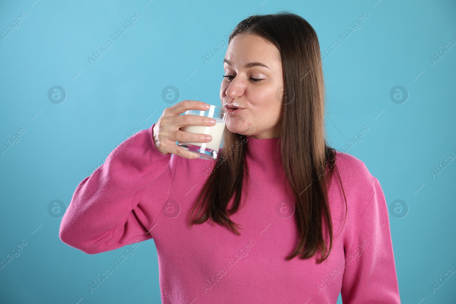 Photo of Happy woman with milk mustache holding glass of drink on light blue background