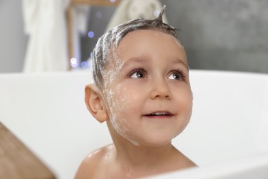 Cute little boy washing hair with shampoo in bathroom