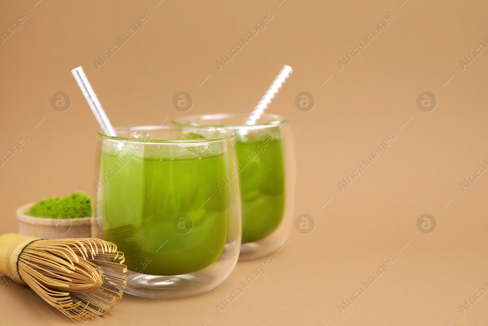 Photo of Delicious iced green matcha tea, powder and bamboo whisk on pale brown background, space for text