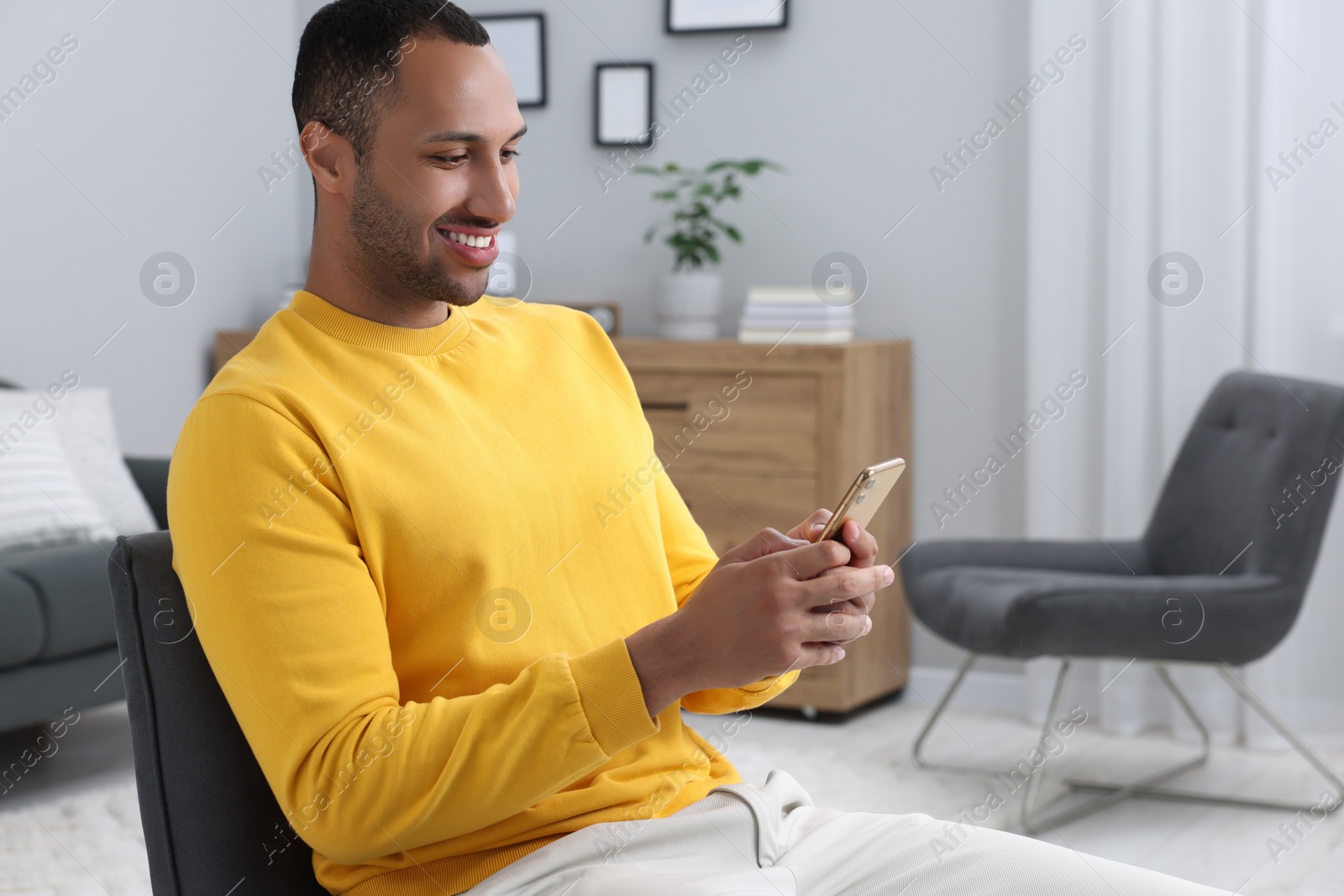 Photo of Happy man sending message via smartphone indoors