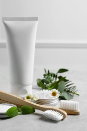 Bamboo toothbrushes, tube of cream and herbs on light grey table