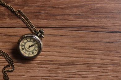 Pocket clock with chain on wooden table, top view. Space for text