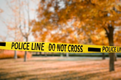 Image of Yellow police tape isolating crime scene. Blurred view of autumn city park 
