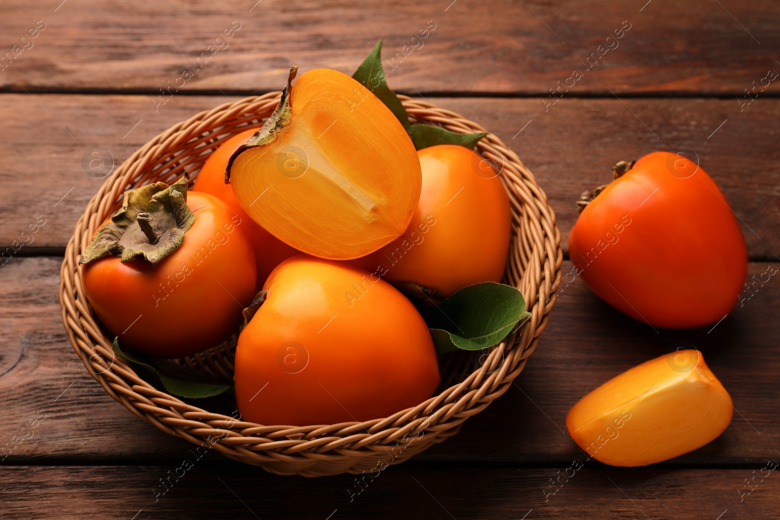 Photo of Delicious ripe persimmons in wicker basket on wooden table