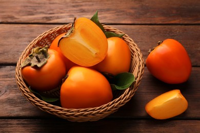 Photo of Delicious ripe persimmons in wicker basket on wooden table