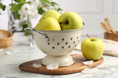 Photo of Colander with fresh apples and flower petals on white marble table