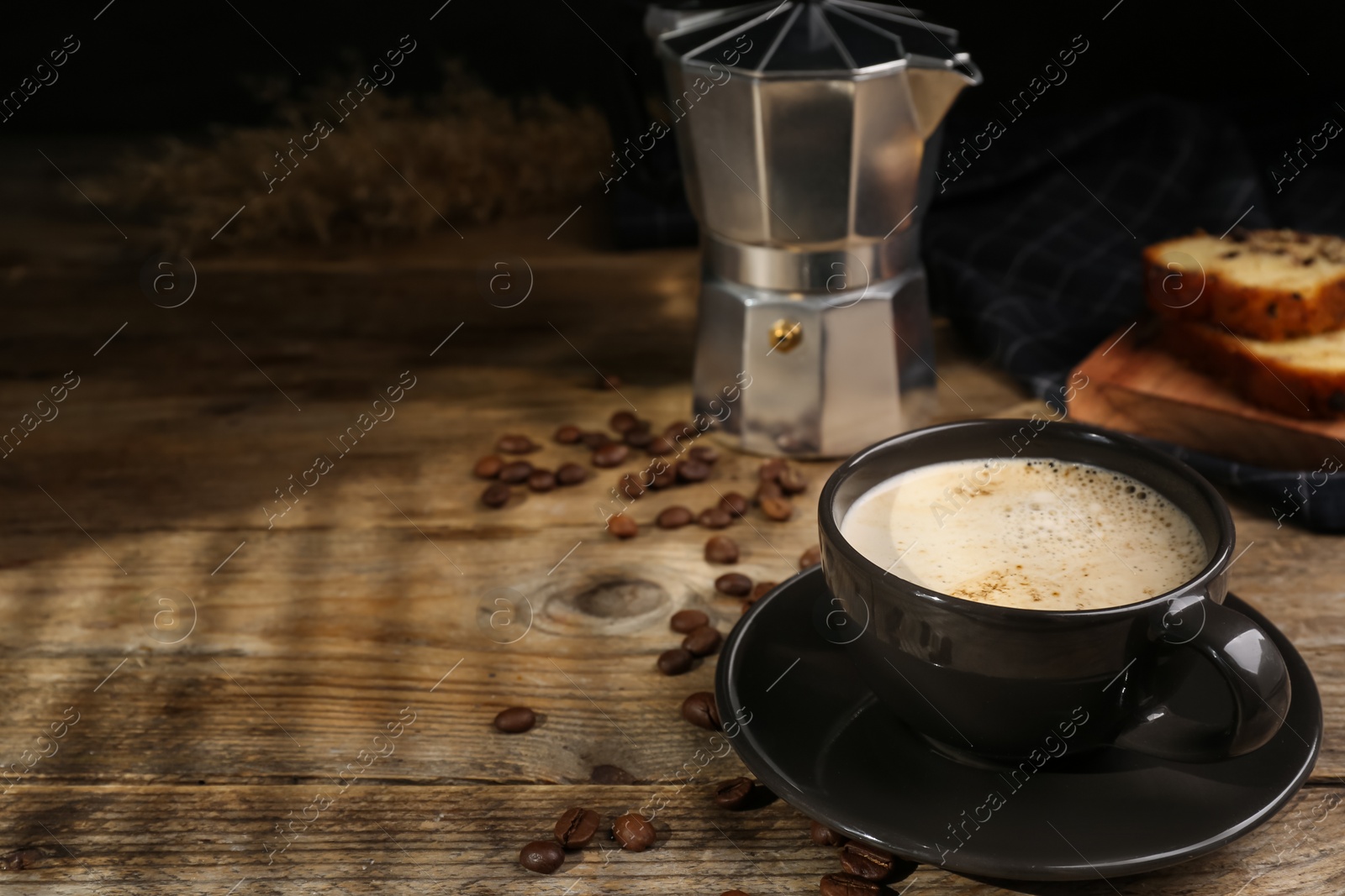 Photo of Cup of aromatic coffee, moka pot and scattered beans on wooden table. Space for text