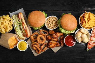 Photo of Burgers, onion rings and other fast food on black wooden table, flat lay
