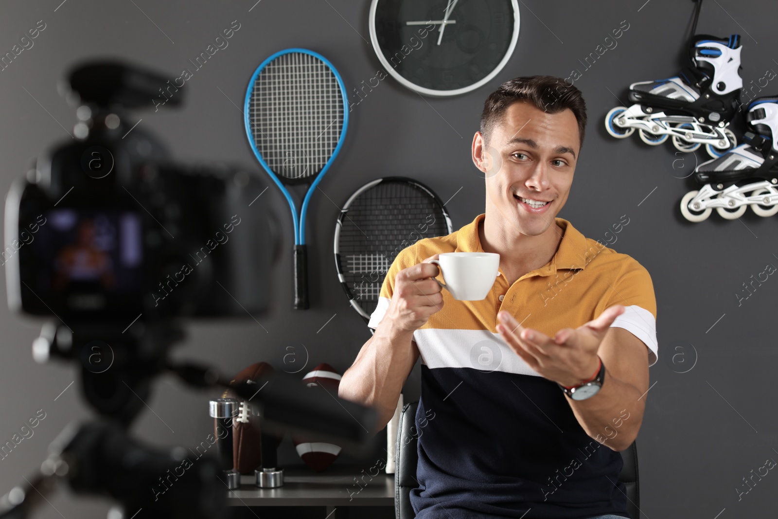 Photo of Sport blogger with cup of coffee recording video on camera at home