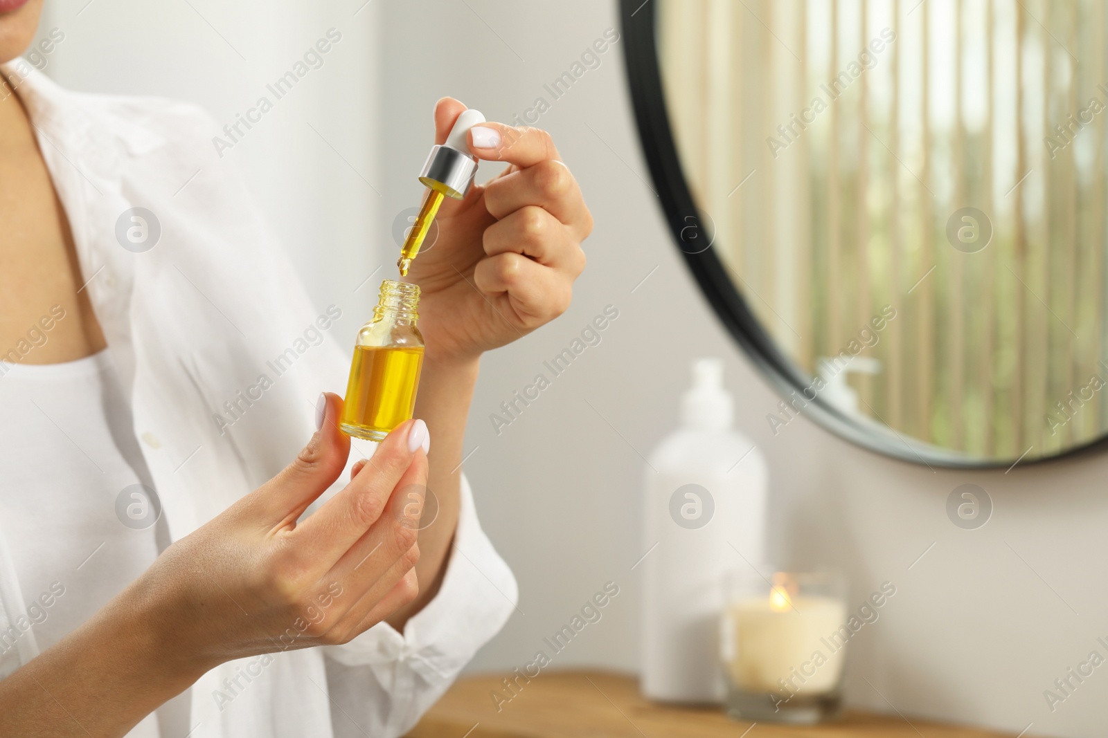 Photo of Young woman with bottle of essential oil indoors, closeup